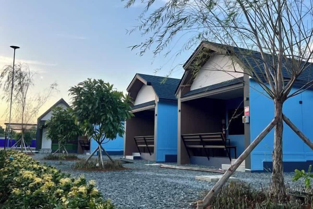 A row of blue buildings with open garages, surrounded by gravel and plants.