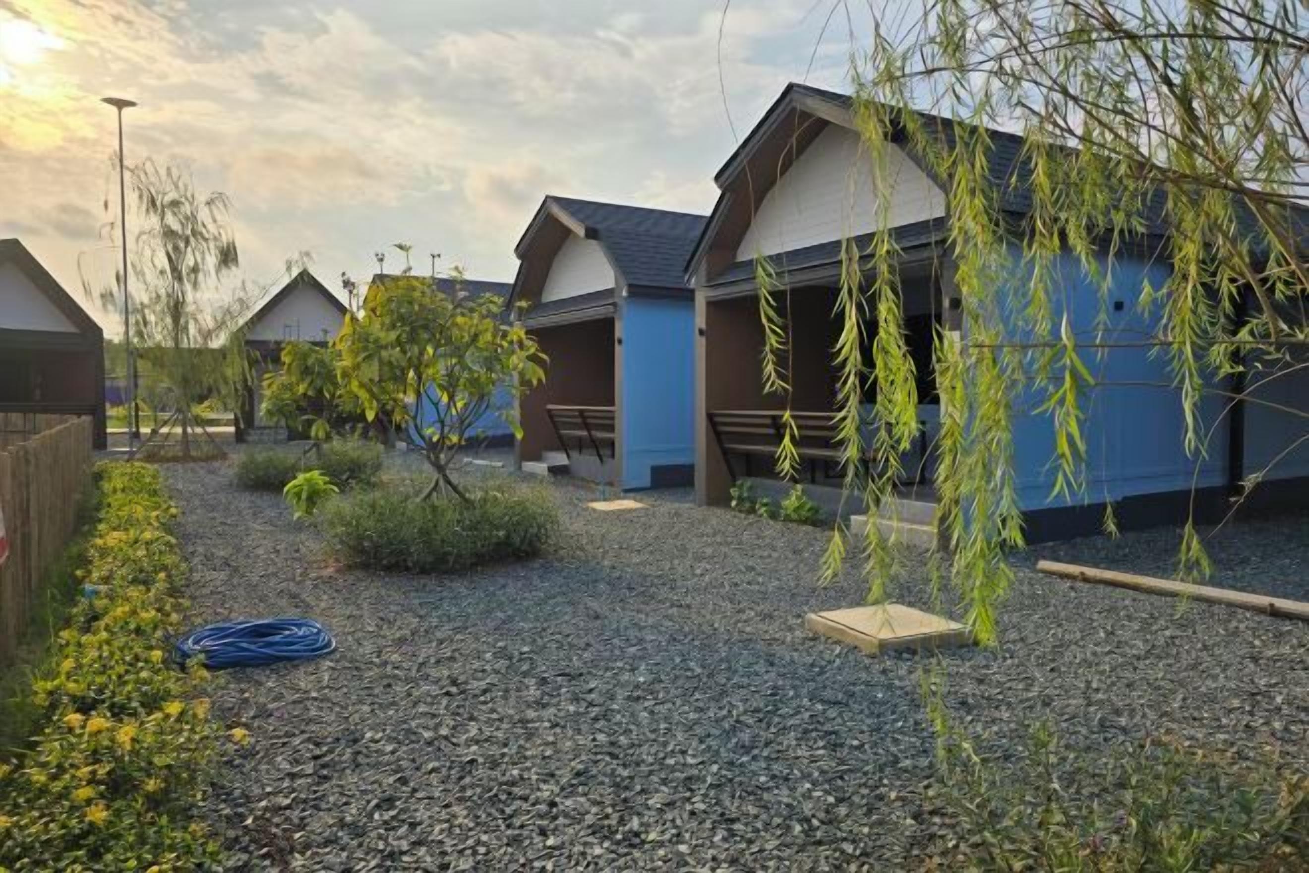 A courtyard with multiple buildings, gravel ground, and some greenery.
