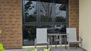 Un patio con una mesa, dos sillas, un muro de ladrillo y un ventanal grande.