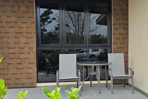 A patio area with a table and two chairs, a brick wall, and a large window. - Napdown Resort Trat (Trat)