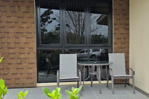 A patio area with a table and two chairs, a brick wall, and a large window.