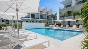 A modern hotel with a swimming pool, white lounge chairs, and umbrellas.