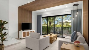 A modern living room with a flat-screen TV, sofas, a coffee table, and a large sliding glass door leading to an outdoor area.