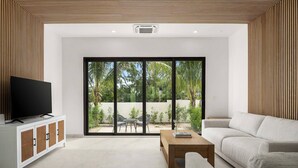 A modern living room with a television, sofa, coffee table, and a sliding glass door leading to an outdoor area.