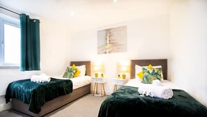 Ein Hotelzimmer mit zwei Betten, jeweils mit grüner Bettdecke und passenden Kissen, einem kleinen Nachttisch mit Lampe und einem Bild an der Wand.