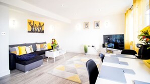 Een moderne woonkamer met een grijze bank, een witte salontafel en een televisie op een dressoir.