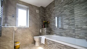 Ein modernes Badezimmer mit einer großen Badewanne, einer Toilette und einem Fenster.