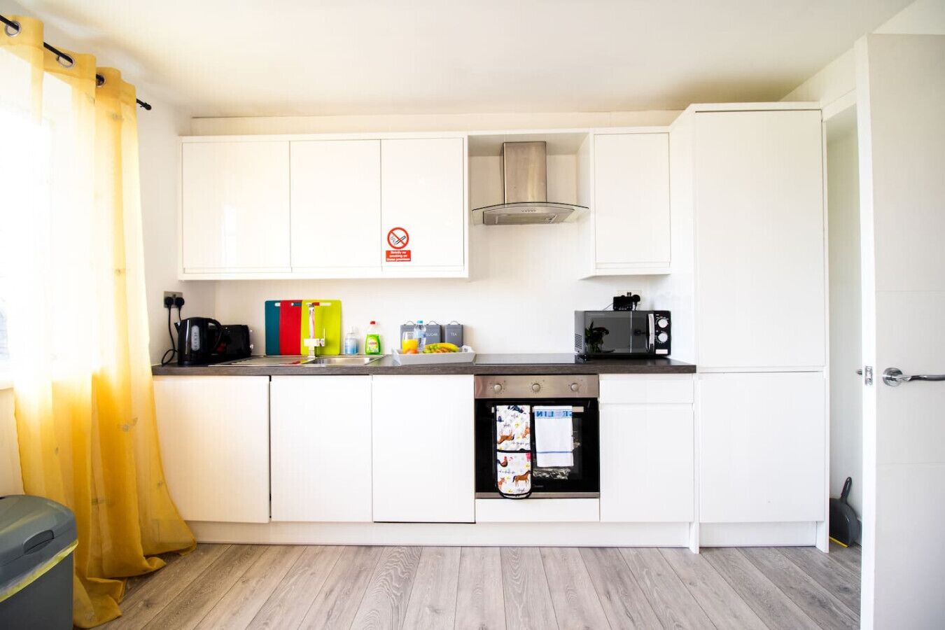A compact kitchen with white cabinets, a stainless steel range hood, a microwave, and a dishwasher.