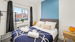 Habitación de hotel con cama, ventana con cortinas, mesita de noche con lámpara y vista a la calle.