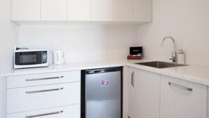 Eine kompakte Küche mit Mikrowelle, Kühlschrank, Spüle und weißen Schränken.
