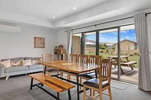 A spacious living room with a large wooden dining table, comfortable seating, and a sliding glass door leading to an outdoor patio. - Hunter Hunter (Lake Tekapo)