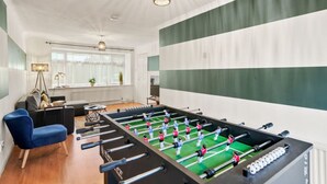 A modern living room with a foosball table, a blue armchair, and a sofa.