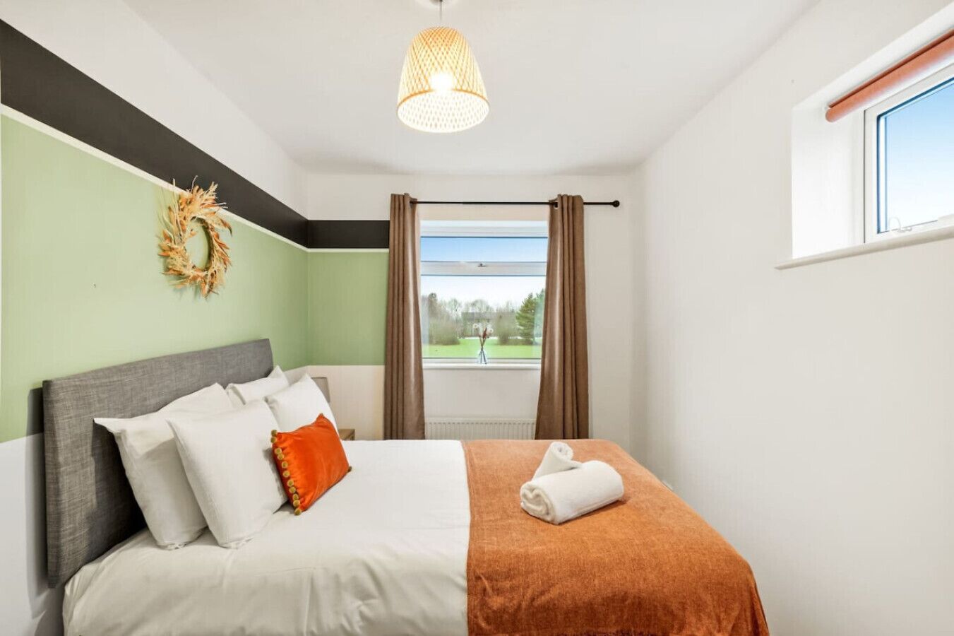 A bedroom with a bed, a view of a park, and a window with curtains.