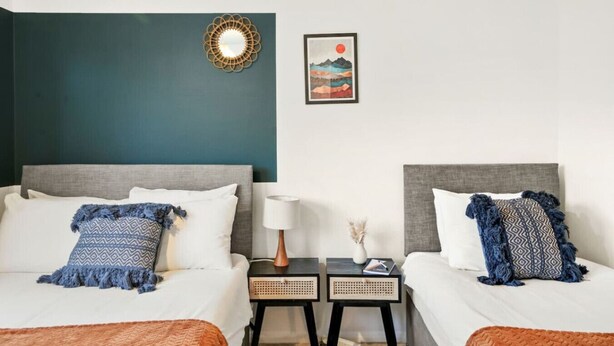 A hotel room with two beds, a nightstand with a lamp, and a framed picture on the wall.