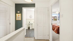 A hallway leading to a bathroom with a sink and a door to a bedroom.