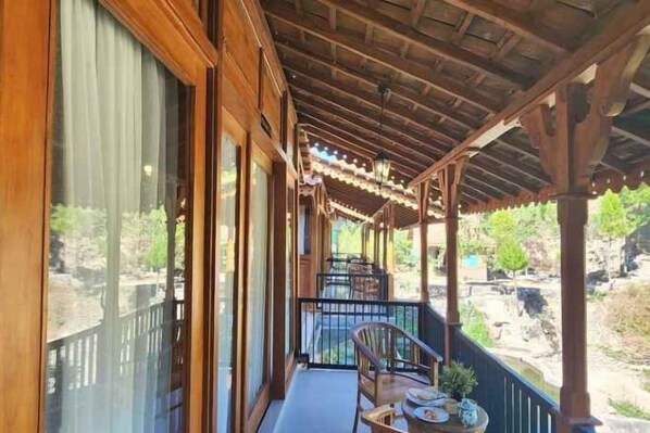 A wooden balcony with a table and chairs, large windows, and a view of a rocky landscape. - Imah Kayu by Horison (Cilimus)