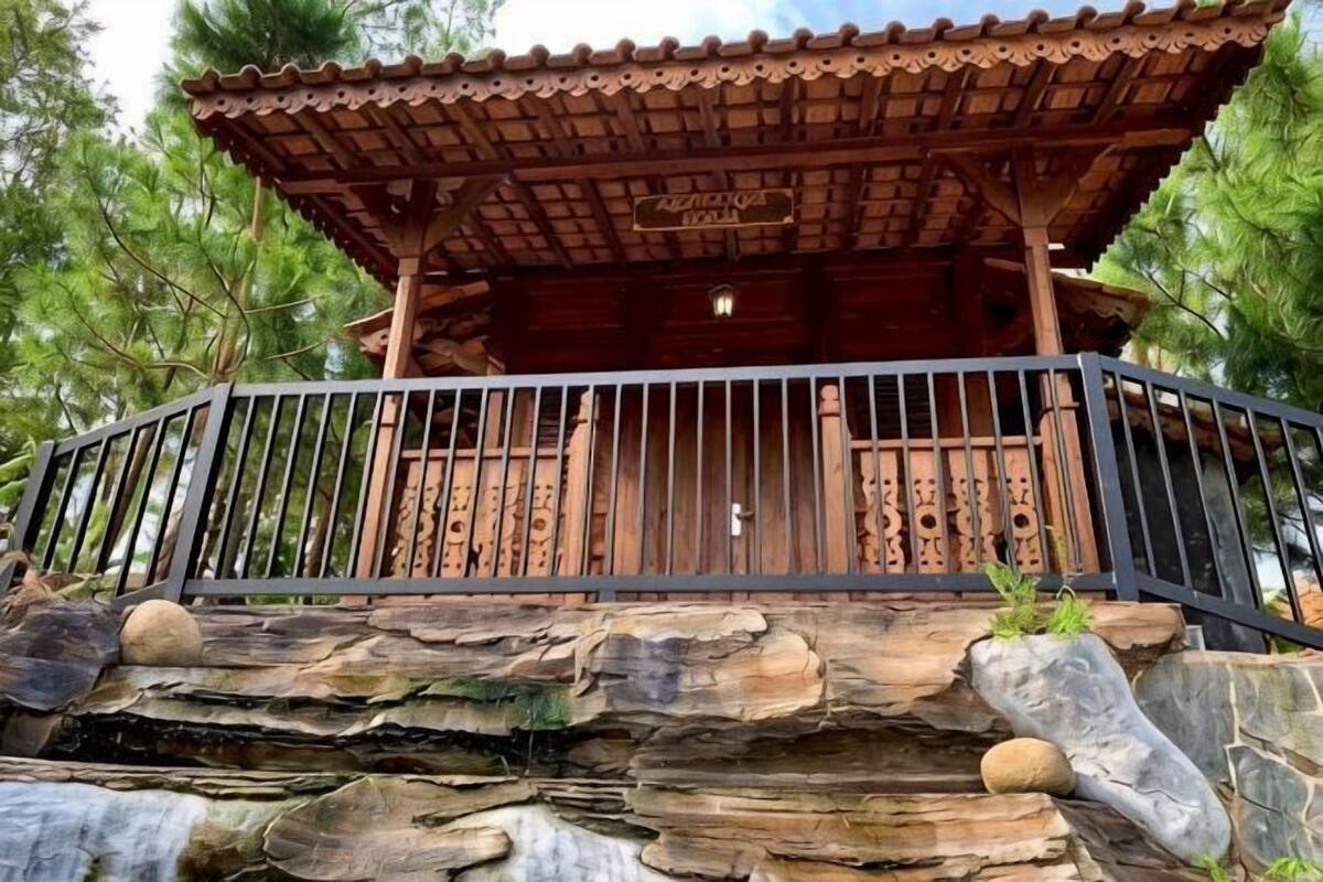 Ein hölzerner Pavillon mit Metallgeländer, auf einem Steinfundament und mit natürlicher Umgebung.