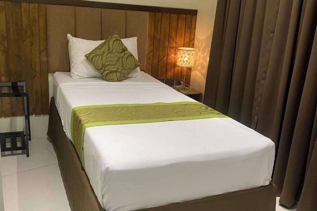 A neatly made bed with a green bedspread, a wooden headboard, and a nightstand with a lamp.