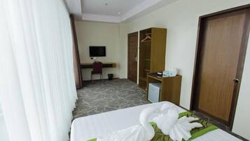 A hotel room with a bed, a desk, a chair, a television, and a wardrobe.