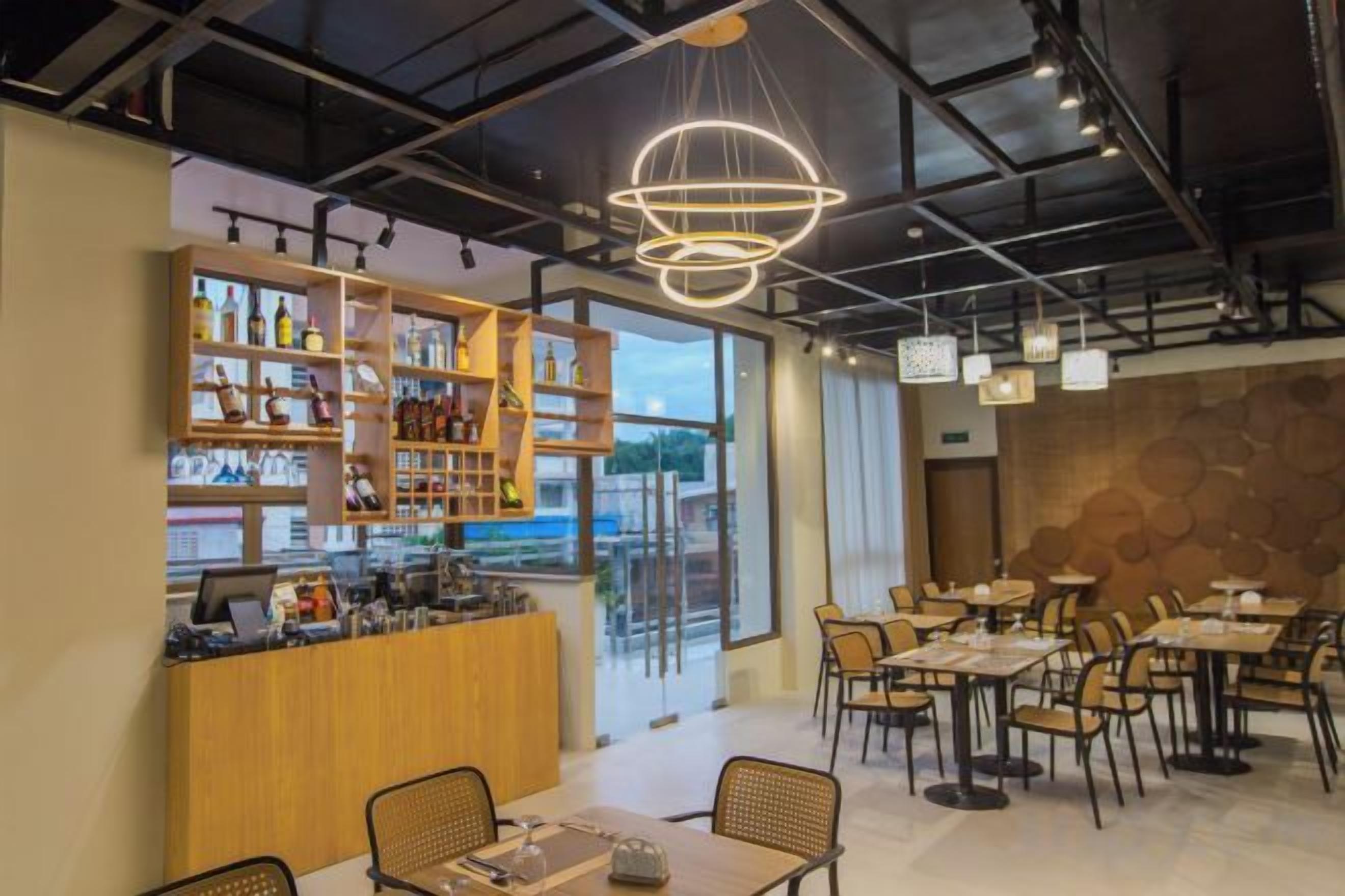 Un café moderno con zona de bar, disposición de mesas y vistas a través del ventanal.