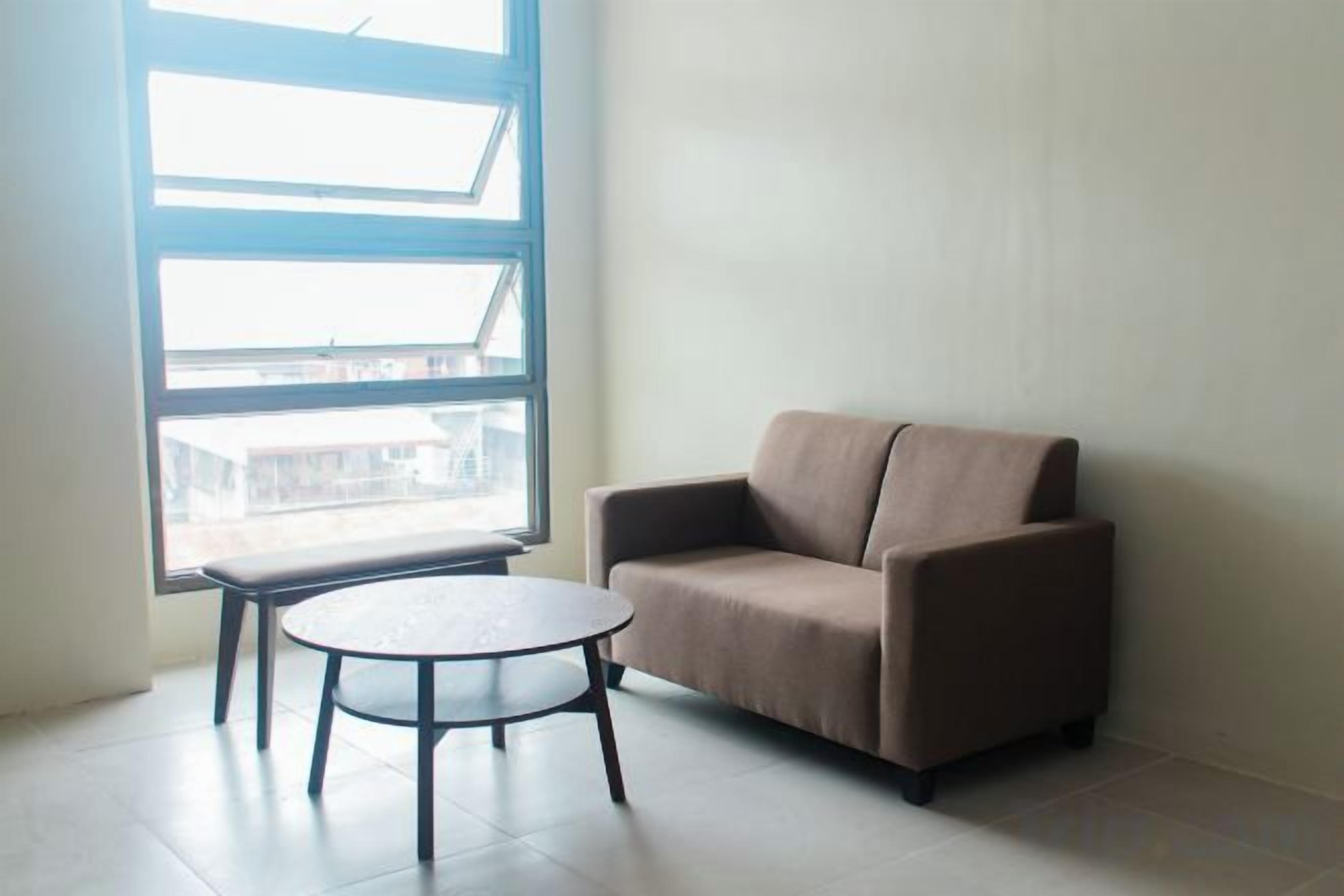 A room with a sofa and a small table, a large window, and a view of buildings outside.