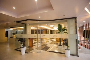 Un hall d’hôtel avec une entrée en verre, des plantes en pot et un sol à carreaux.