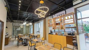A café with tables and chairs, a counter with shelves of items, and large windows.