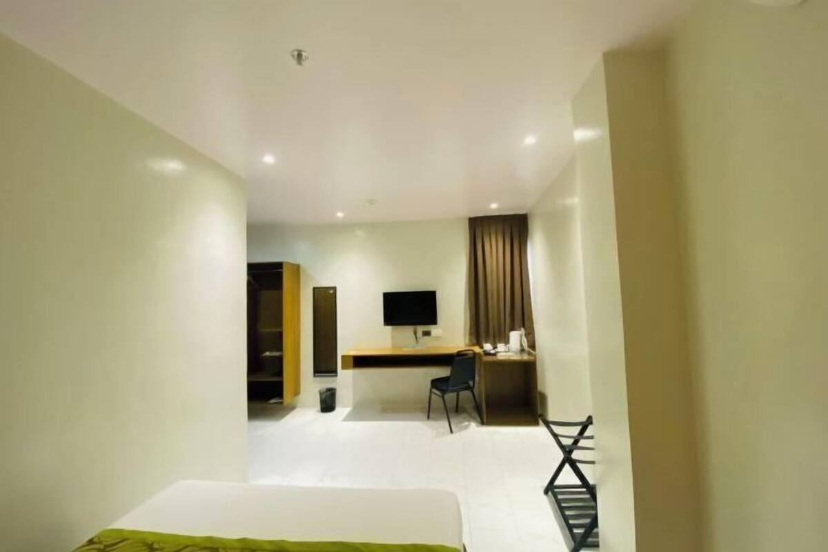 A hotel room with a bed, desk, chair, TV, and a wardrobe.