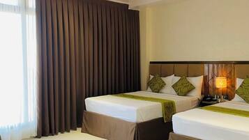 A hotel room with two beds, a large window with curtains, a wooden headboard, and a bedside lamp.