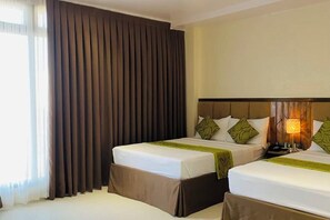A hotel room with two beds, a large window with curtains, a wooden headboard, and a bedside lamp. - Maxi Hotel and Event Center (Tagbilaran)