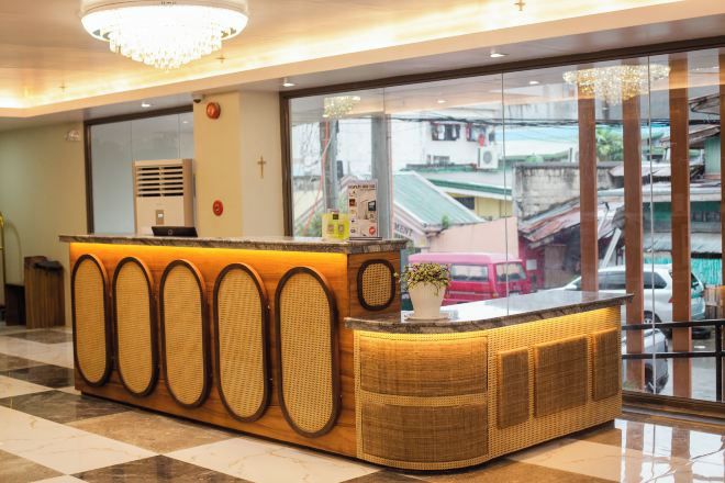 A reception desk with a woven design, a cross on the wall, and a view of the street through a glass window.