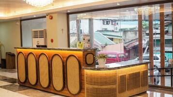 A reception desk with a woven design, a cross on the wall, and a view of the street through a glass window.