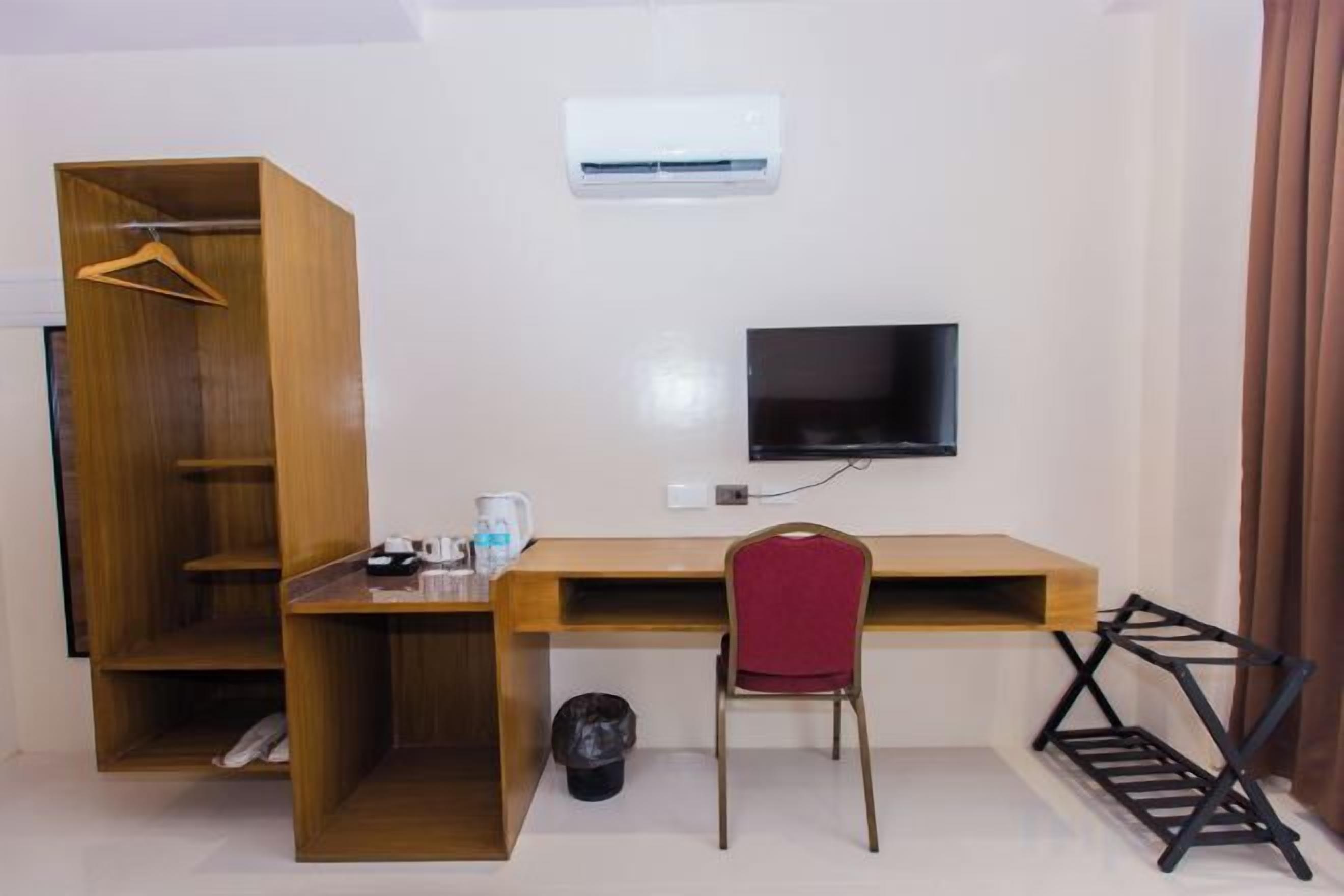 A room with a wooden desk, a red chair, a TV, and a wardrobe.