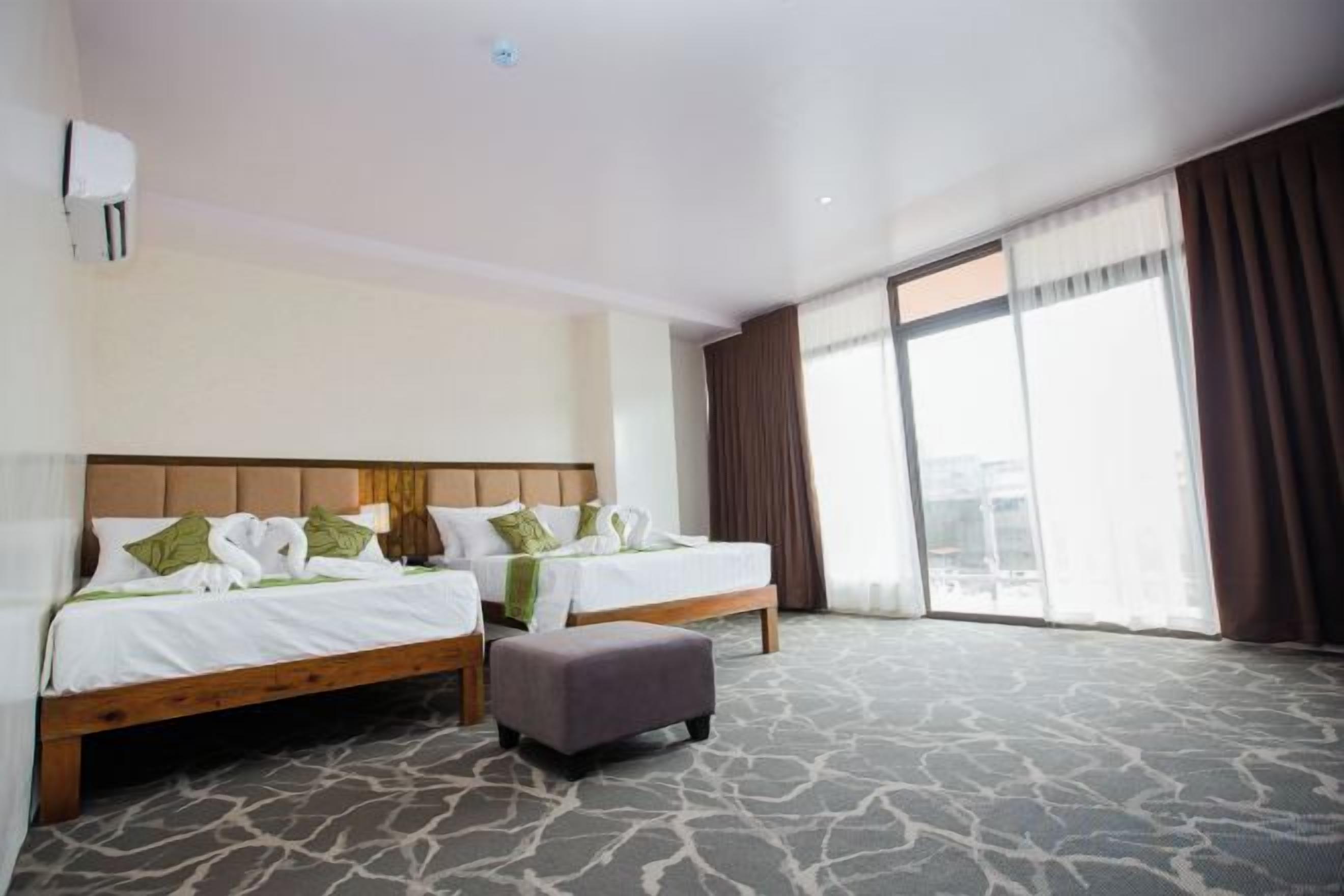 Habitación de hotel con dos camas, un ventanal grande y piso alfombrado.