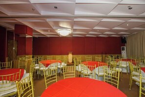 A banquet hall with round tables and chairs, a stage, and a red wall. - Maxi Hotel and Event Center (Tagbilaran)