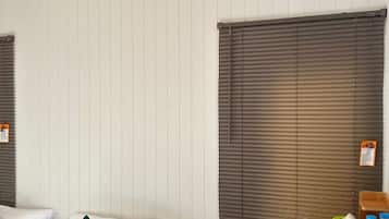 A hotel room with two beds, a window with blinds, and a small table with a green suitcase and toiletries.
