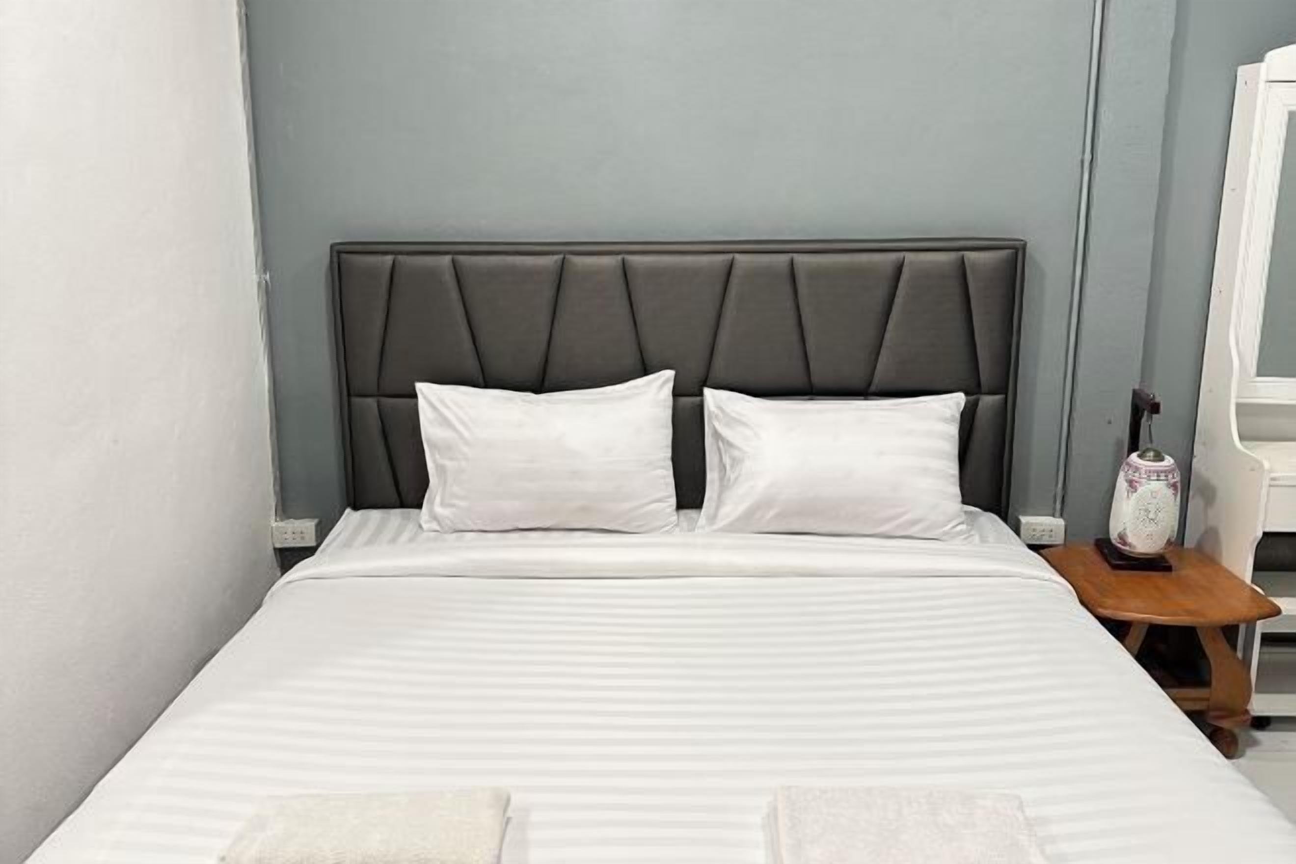 A bed with a headboard, two pillows, a bedside table with a lamp, and a nightstand.