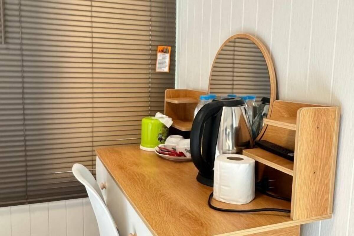 Una encimera de madera con una tetera, una taza verde, un plato con cubiertos y un rollo de papel higiénico.