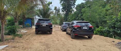 A dirt road with parked cars and a small building on the left.