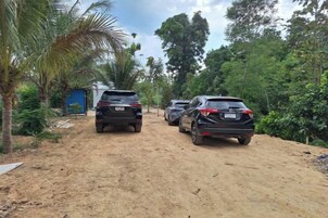A dirt road with parked cars and a small building on the left.