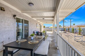 Relax on the covered patio, surrounded by lush greenery and a small pool, with a bench and dining area nearby.