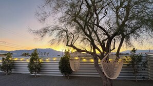 Ein Baum mit zwei Hängematten, die an seinen Ästen befestigt sind, vor einer Berglandschaft und einem Sonnenuntergang.