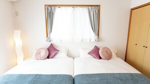 Cama doble con dos almohadas, mesita de noche, lámpara y ventana con cortinas.