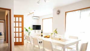 Un comedor luminoso con una mesa blanca, sillas y un televisor.