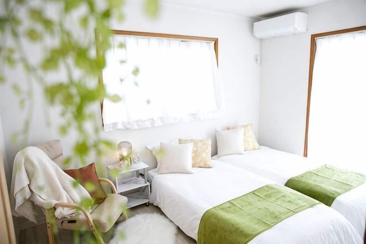 A bedroom with two beds, a bedside table, a chair, and a window with curtains.