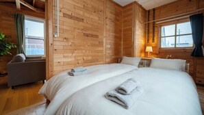Een kamer met houten lambrisering, een groot bed, een bank, een lamp en een raam met gordijnen.