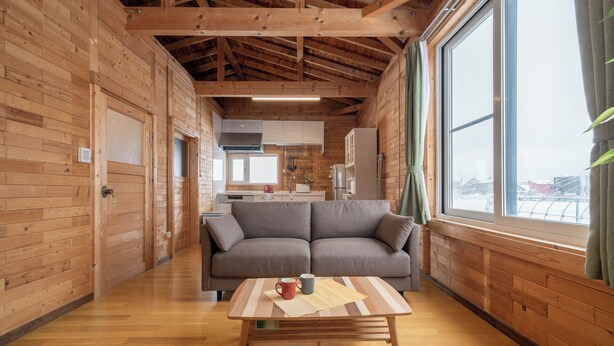 Een houten interieur met een bank, een tafel met een mok en een onderzetter, en een keuken op de achtergrond.