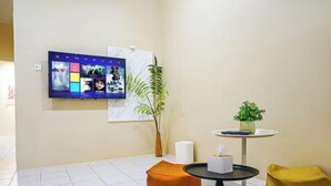 Quarto moderno com televisão de tela plana na parede exibindo pôsteres de filmes, uma mesa redonda pequena com um vaso de plantas verdes e uma poltrona de feijão amarela.