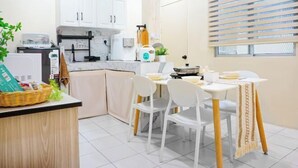 Uma cozinha compacta com armários brancos, uma mesa de jantar com cadeiras e uma janela com persianas.