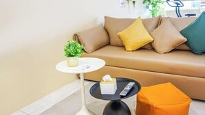 Uma sala de estar moderna com um sofá bege, uma mesa redonda pequena, uma planta em vaso e um controle remoto sobre a mesa.